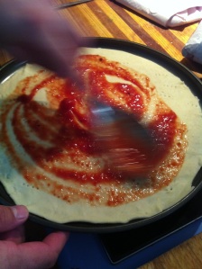 A ladle full of pizza sauce, spread with back of spoon